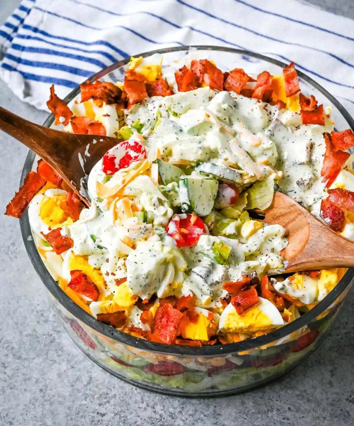 This classic Seven Layer salad is layered with iceberg lettuce, smoky bacon, hard-boiled eggs, sharp cheddar cheese, fresh veggies, and your choice of peas or garbanzo beans, plus creamy avocado. It's the ultimate make-ahead side dish, perfect for BBQs or family dinners. This easy, crowd-pleasing 7 Layer Salad is topped with a generous drizzle of homemade ranch dressing. This easy, crowd-pleasing layered salad is a beautiful, delicious side dish!