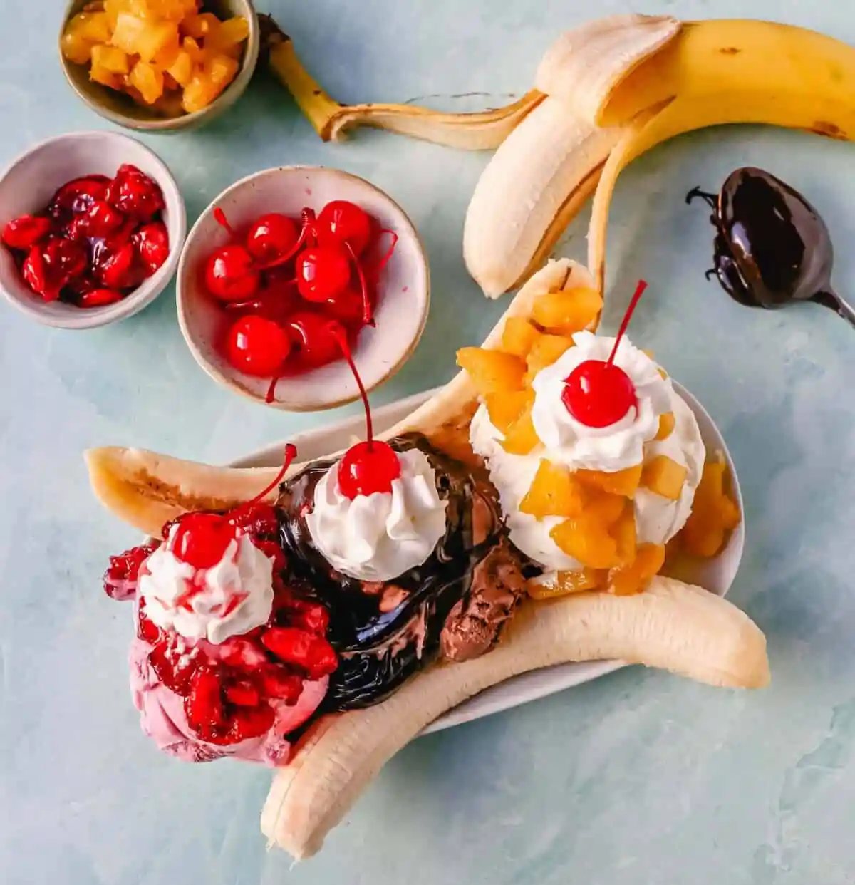 A classic Banana Split recipe made with fresh bananas, chocolate ice cream with hot fudge sauce, strawberry ice cream with strawberry sauce, vanilla ice cream with pineapple sauce, whipped cream, and cherry.