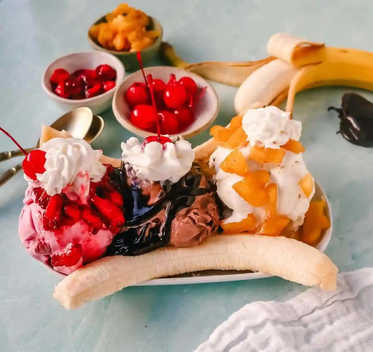 A classic Banana Split recipe made with fresh bananas, chocolate ice cream with hot fudge sauce, strawberry ice cream with strawberry sauce, vanilla ice cream with pineapple sauce, whipped cream, and cherry.