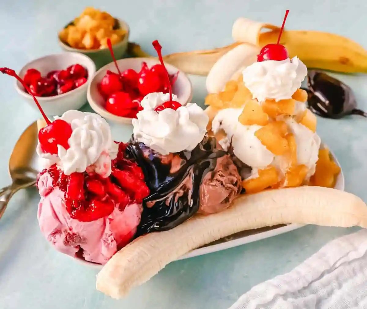 A classic Banana Split recipe made with fresh bananas, chocolate ice cream with hot fudge sauce, strawberry ice cream with strawberry sauce, vanilla ice cream with pineapple sauce, whipped cream, and cherry.