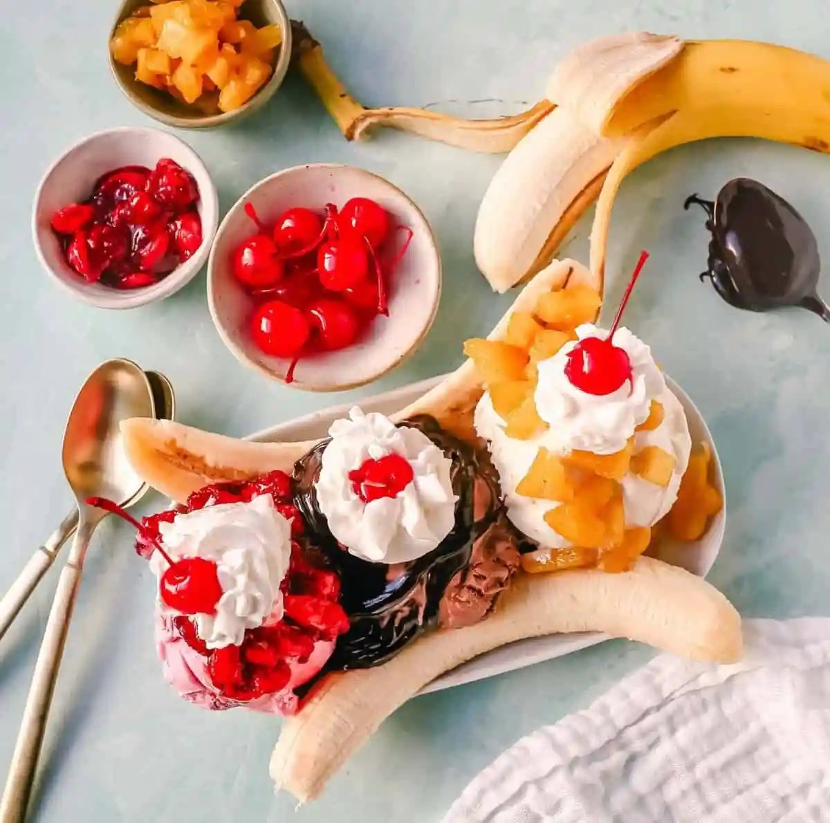 A classic Banana Split recipe made with fresh bananas, chocolate ice cream with hot fudge sauce, strawberry ice cream with strawberry sauce, vanilla ice cream with pineapple sauce, whipped cream, and cherry.