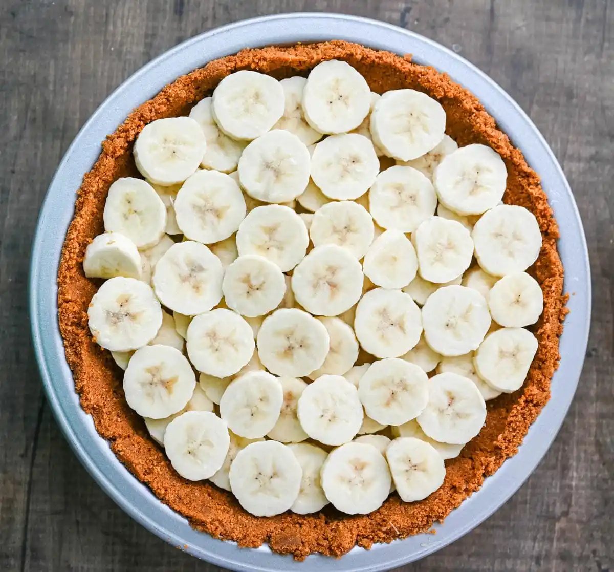 Placing bananas on top of toffee to make banoffee pie.
