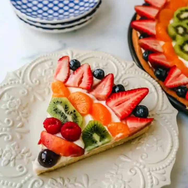 Fruit Pizza with a Sugar Cookie Crust is made with a large, pizza-sized baked sugar cookie and topped with a sweet cream cheese whipped cream and sprinkled with glazed fresh fruit.