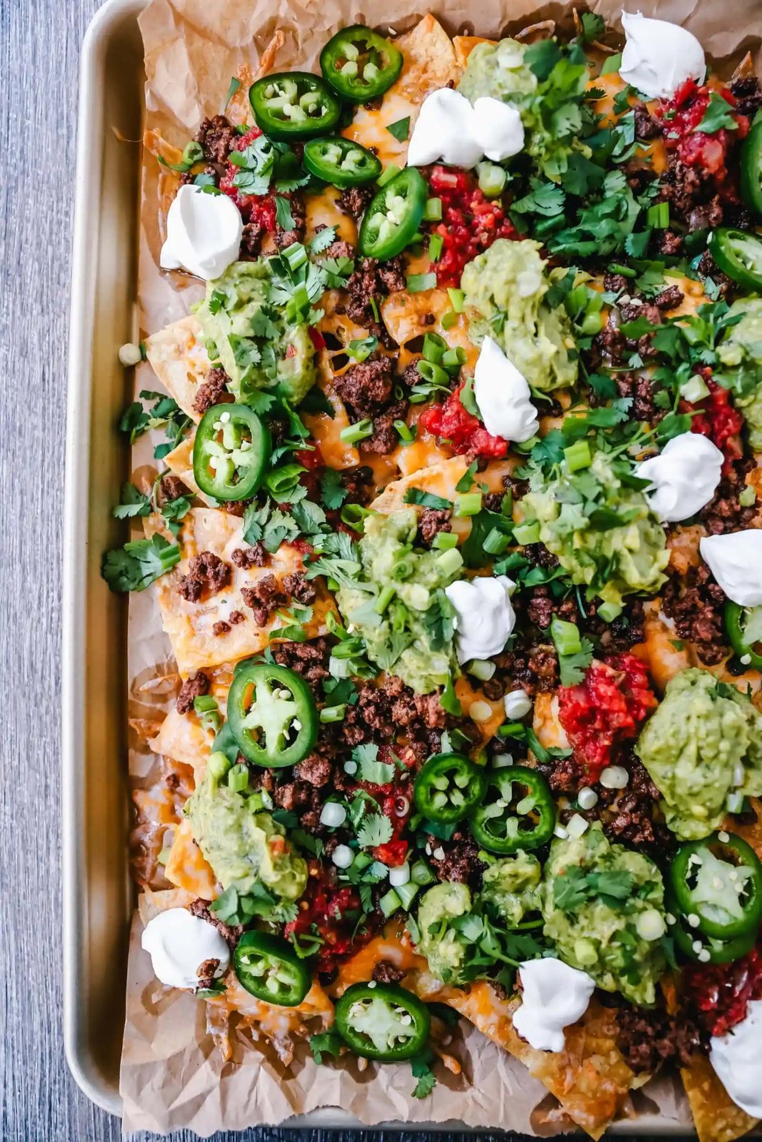 Ground Beef Nachos Recipe Seasoned ground beef with crispy tortilla chips, Mexican cheeses, fresh guacamole, sour cream, jalapenos, fresh salsa, green onions, and cilantro make the best beef nachos!
