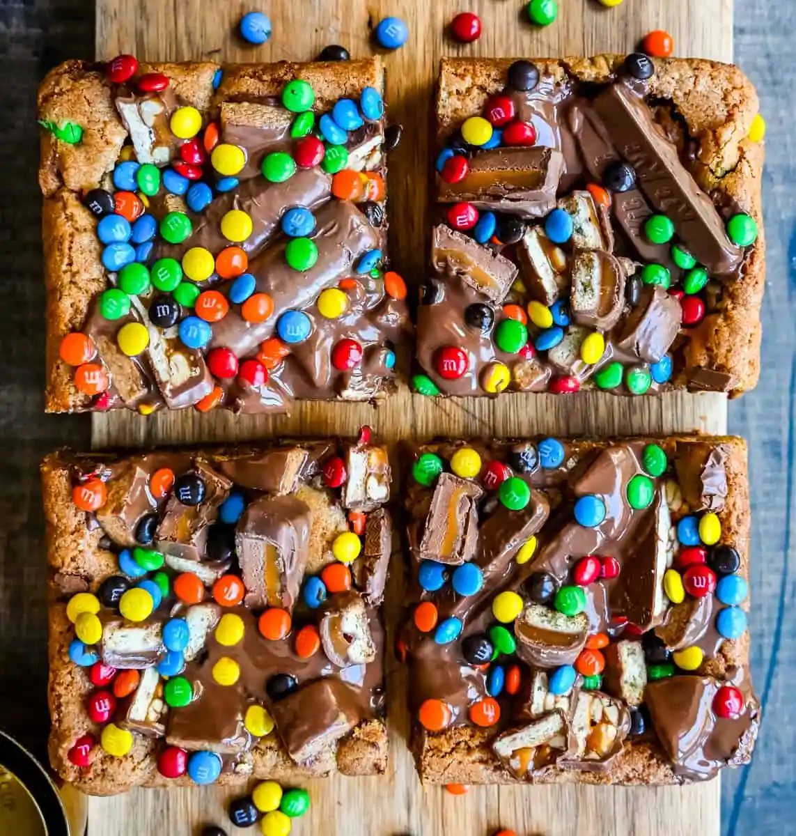 An ooey gooey cookie bar topped with an assortment of candy bars. The perfect candy bar blondie dessert to make with Halloween candy.