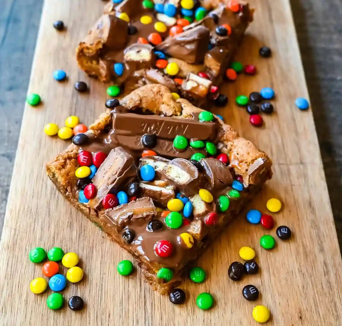 An ooey gooey cookie bar topped with an assortment of candy bars. The perfect candy bar blondie dessert to make with Halloween candy.