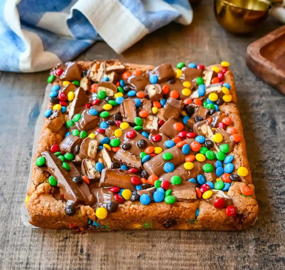 An ooey gooey cookie bar topped with an assortment of candy bars. The perfect candy bar blondie dessert to make with Halloween candy.