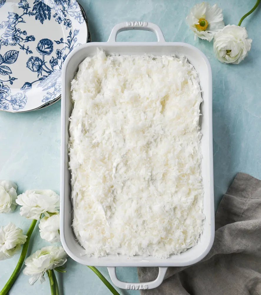 This Coconut Poke Cake is made with a baked cake mix and filled with cream of coconut and sweetened condensed milk and topped with sweet whipped cream and coconut. This Coconut Tres Leches Cake is so easy to make and is perfect for potlucks and parties.