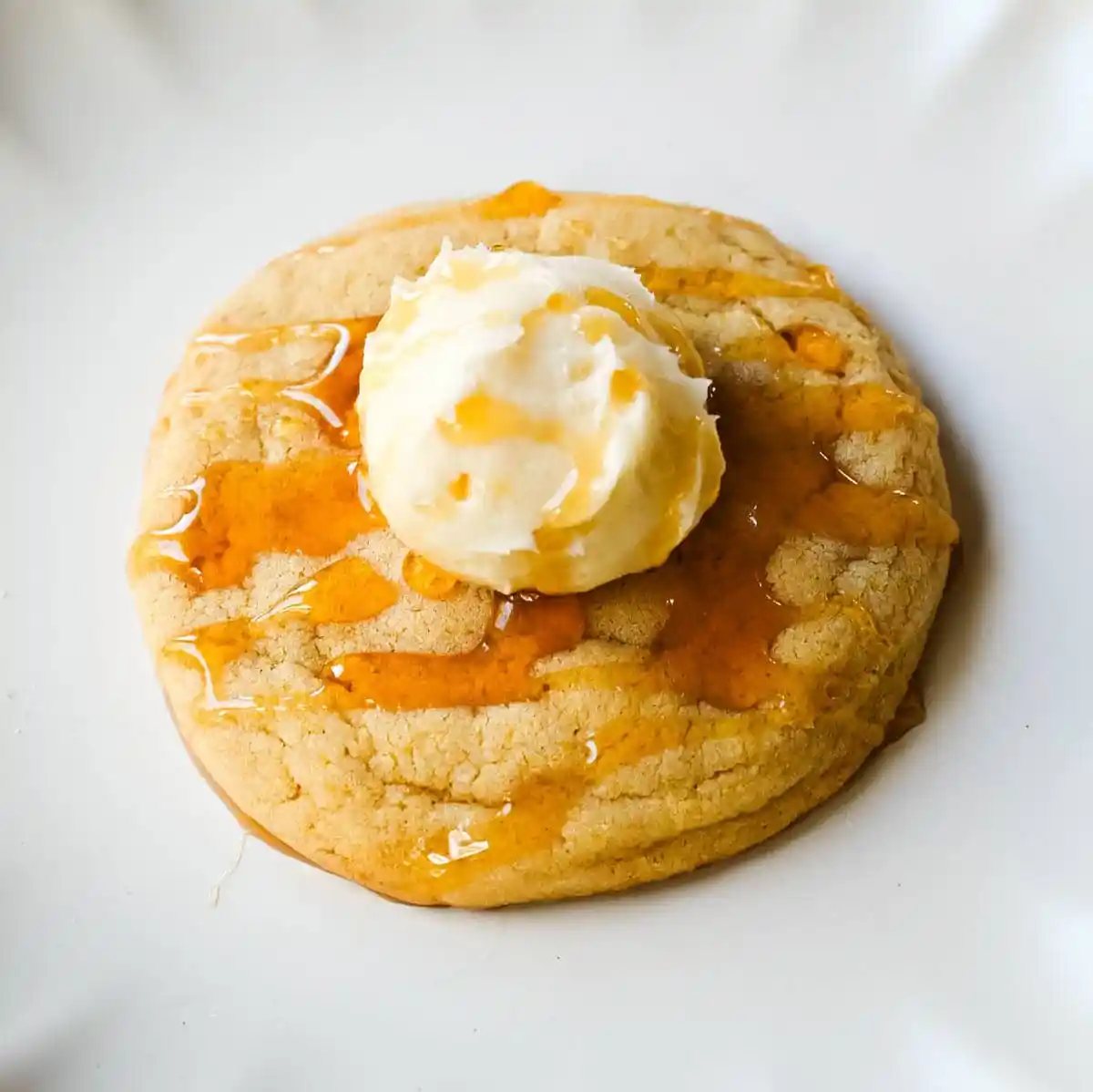Cornbread cookies topped with whipped honey butter and a drizzle of honey on a white plate.