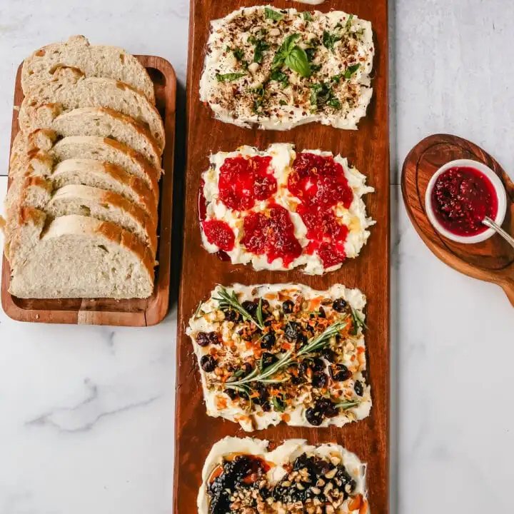 A Butter Board with fresh butter is spread onto a board and topped with an assortment of toppings and served with warm bread. This Butter Board with Toppings is such a fun appetizer for a party! A Butter Board is made by spreading salted, slightly softened butter onto a board and topping it with your favorite toppings like jam and fresh lemon zest and hot honey, walnuts, and fig jam. A savory butter board can be made with butter, roasted garlic, fresh basil, italian seasoning, and red chili flakes. Warm French bread slices are dipped into each savory or sweet butter combination. This Butter Board became famous on TikTok and is now a popular appetizer at parties.