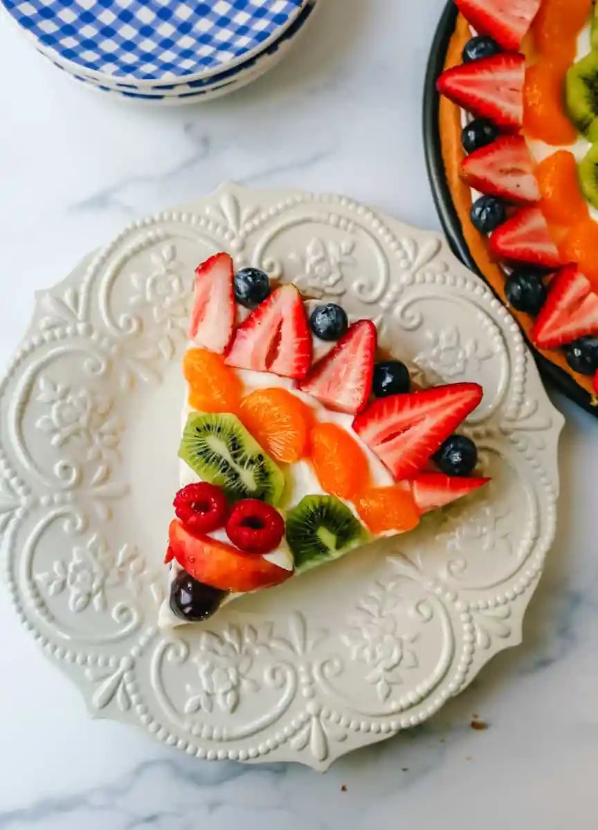 Fruit Pizza with a Sugar Cookie Crust is made with a large, pizza-sized baked sugar cookie and topped with a sweet cream cheese whipped cream and sprinkled with glazed fresh fruit.