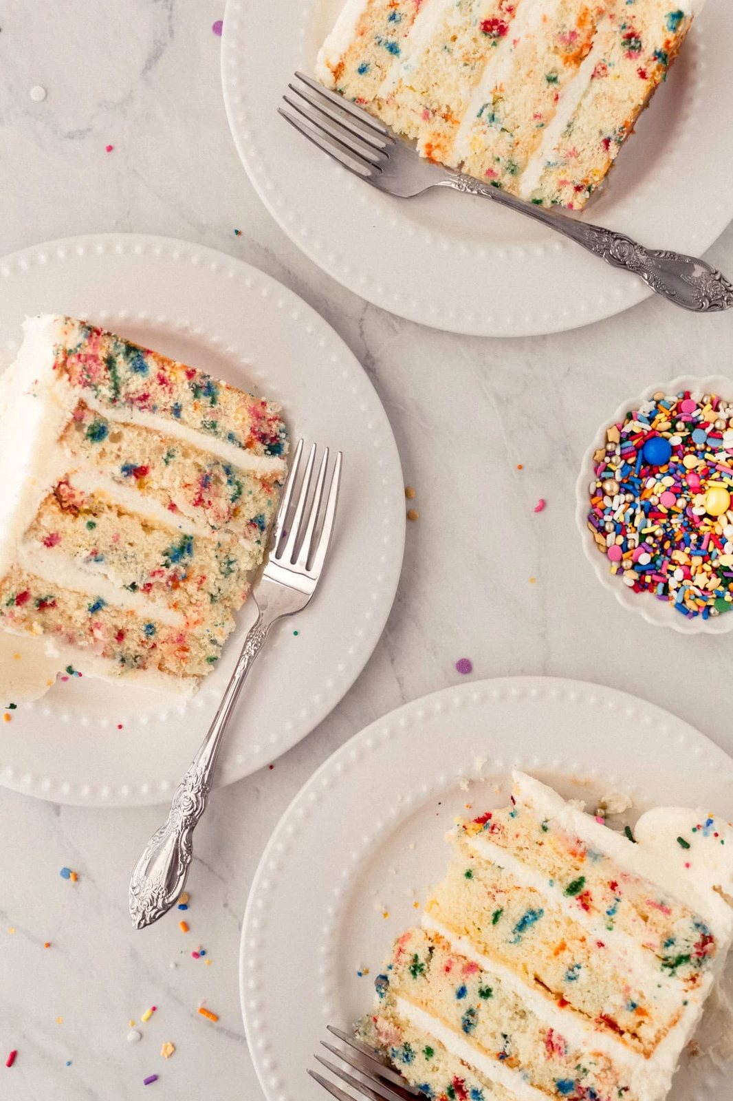 Cut pieces of birthday sprinkle cake. A fluffy homemade Funfetti birthday cake with rainbow sprinkles topped with a light cream cheese buttercream frosting and an array of sprinkles. This Confetti Cake recipe is the perfect birthday cake!