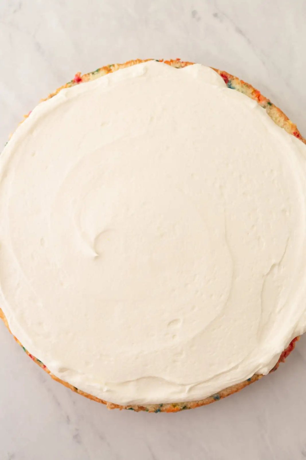 Frosting a homemade funfetti cake or confetti cake with vanilla frosting