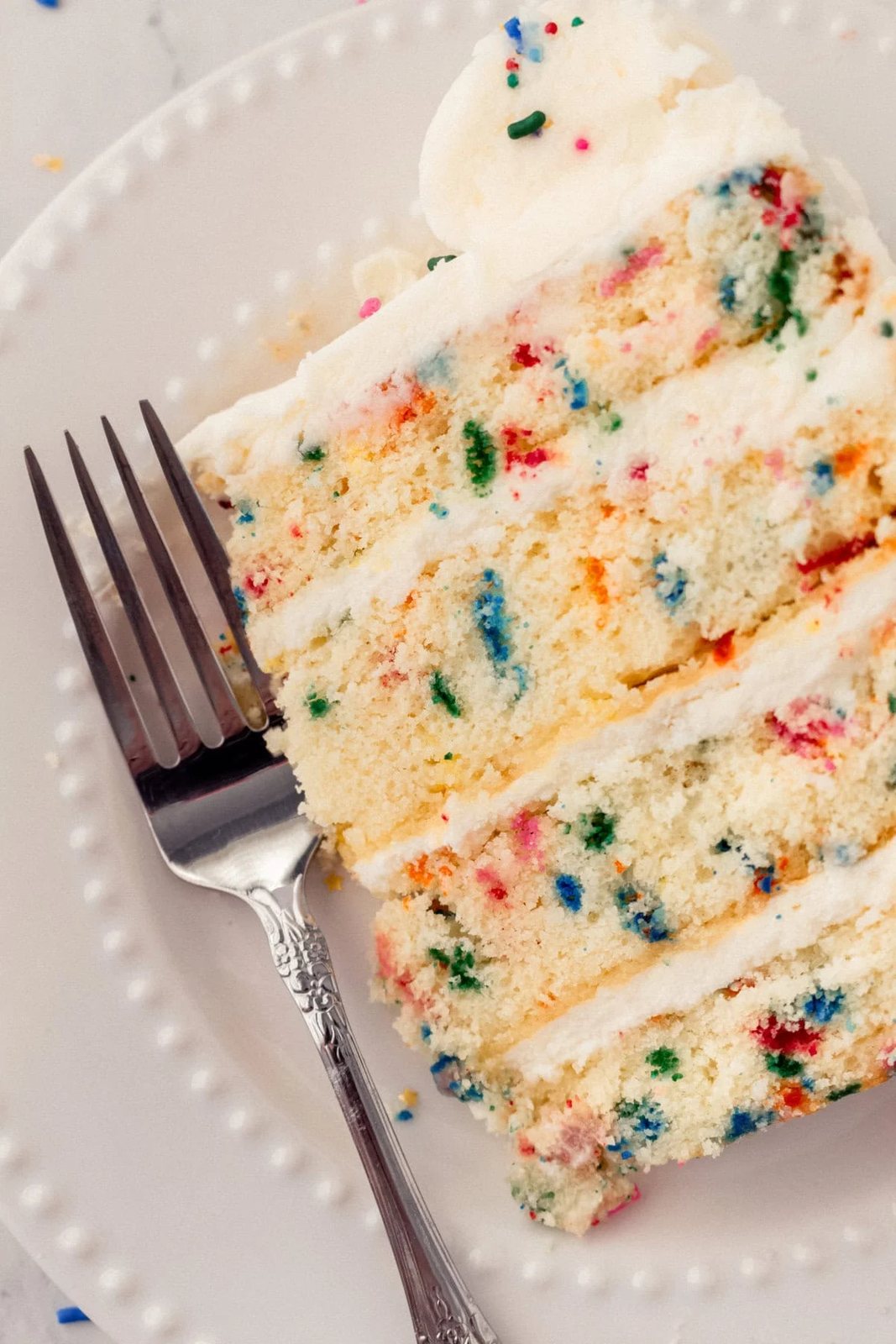 A piece of funfetti or confetti cake with sprinkles. A fluffy homemade Funfetti birthday cake with rainbow sprinkles topped with a light cream cheese buttercream frosting and an array of sprinkles. This Confetti Cake recipe is the perfect birthday cake!