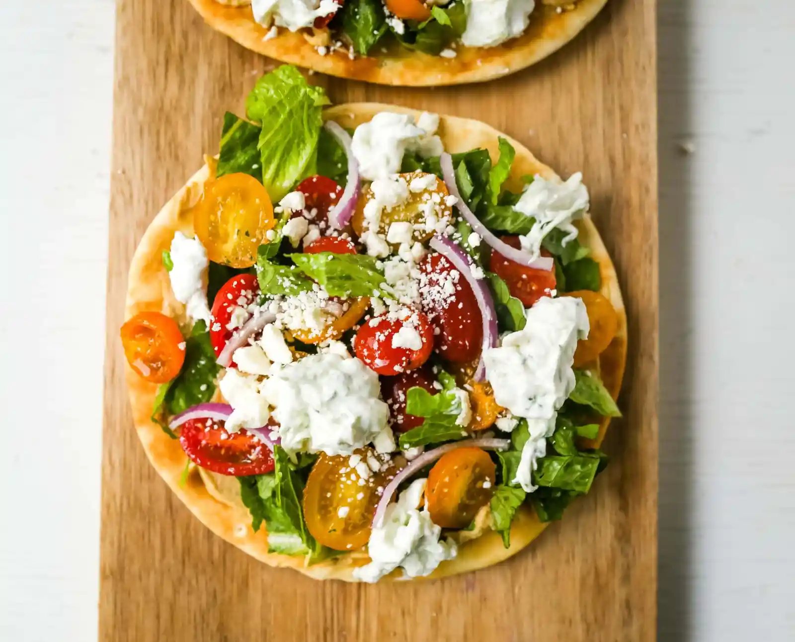 Greek Salad Pita Pizzas Soft pita bread topped with creamy hummus, romaine lettuce, juicy grape tomatoes, feta cheese, red onion, cucumber, and a homemade fresh tzatziki sauce. www.modernhoney.com #greek #greekfood #salad #pita