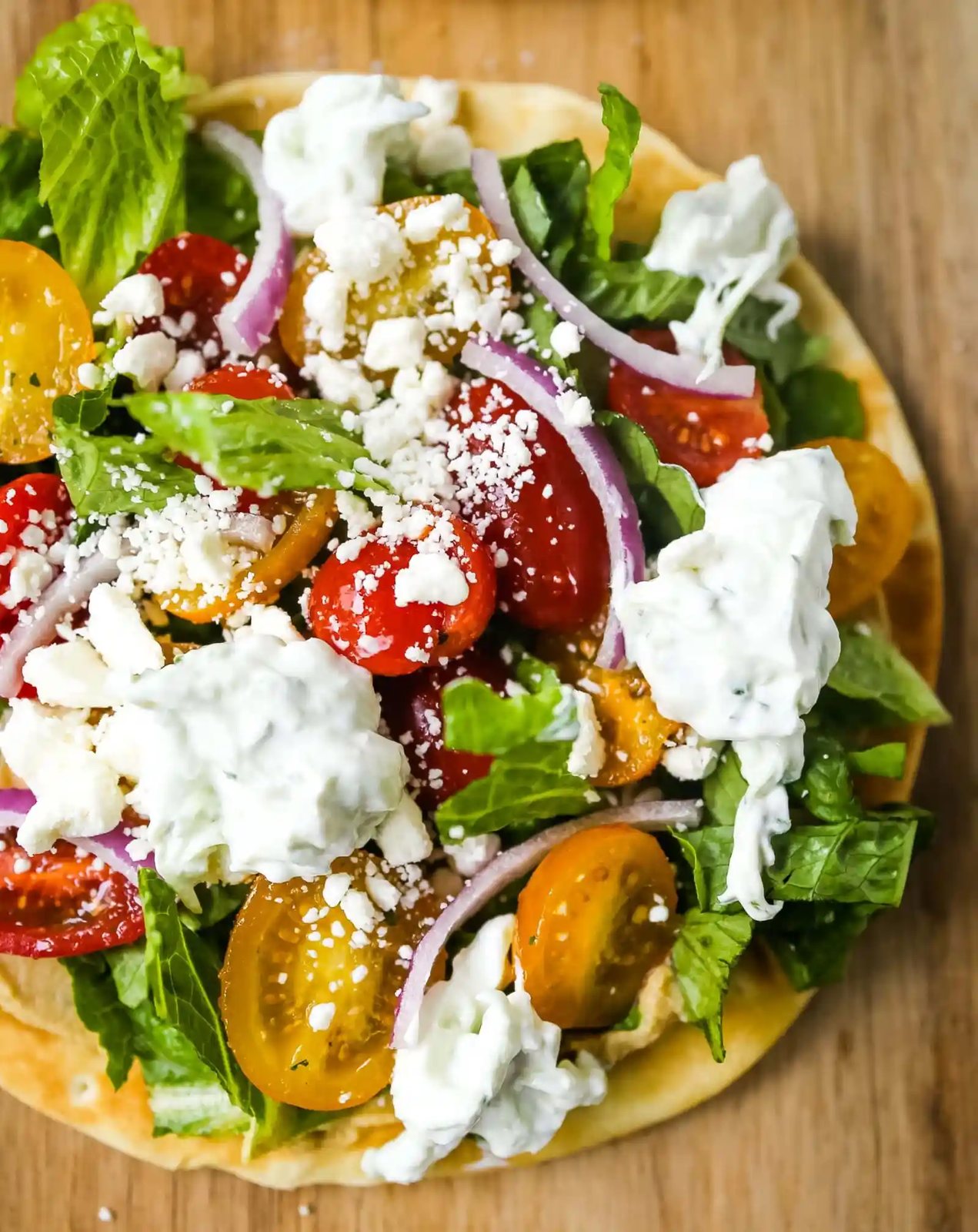 Greek Salad Pita Pizzas Soft pita bread topped with creamy hummus, romaine lettuce, juicy grape tomatoes, feta cheese, red onion, cucumber, and a homemade fresh tzatziki sauce. www.modernhoney.com #greek #greekfood #salad #pita