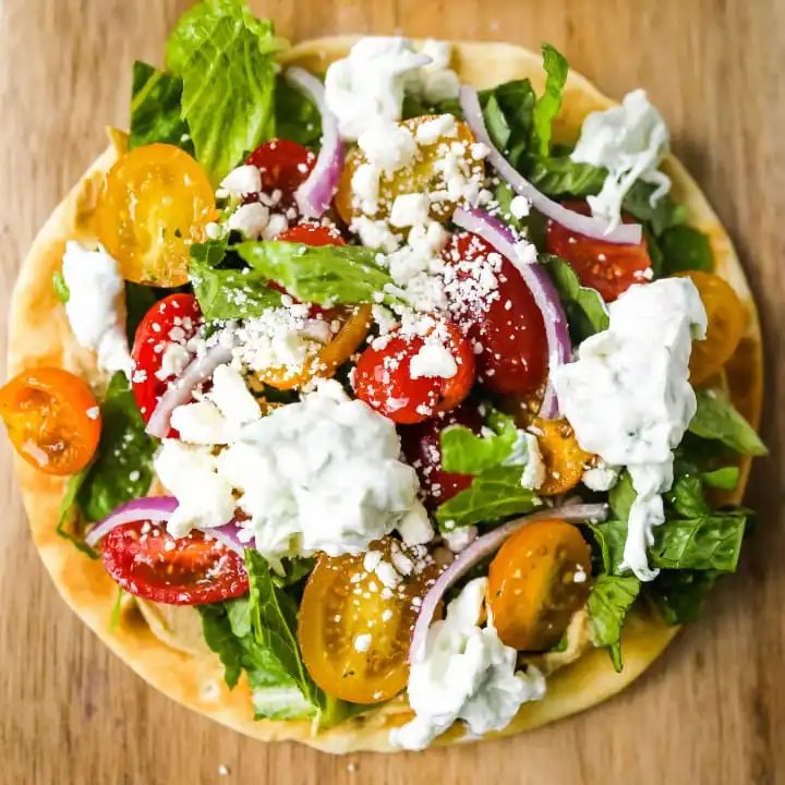 Greek Salad Pita Pizzas Soft pita bread topped with creamy hummus, romaine lettuce, juicy grape tomatoes, feta cheese, red onion, cucumber, and a homemade fresh tzatziki sauce. www.modernhoney.com #greek #greekfood #salad #pita