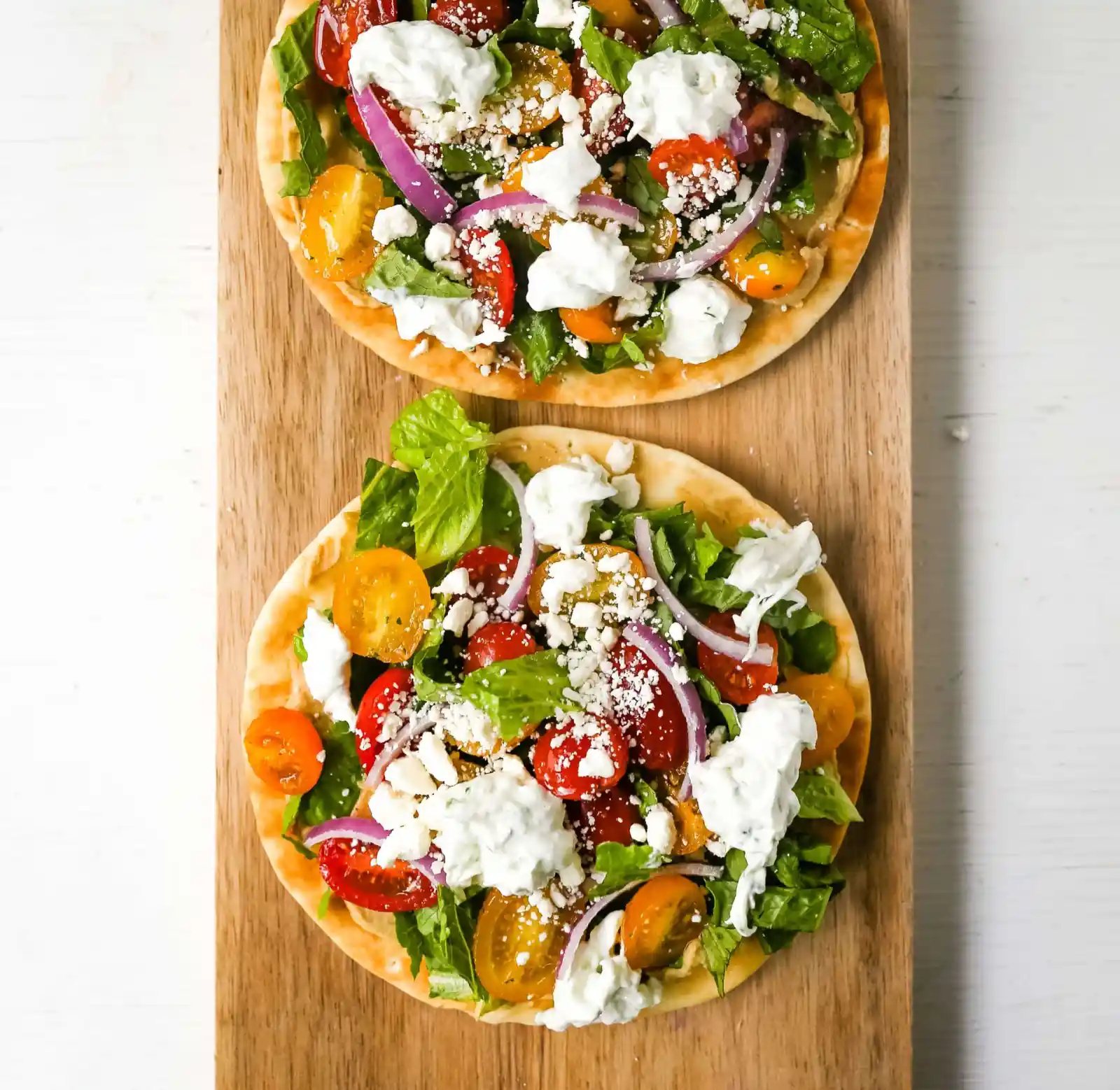 Greek Salad Pita Pizzas Soft pita bread topped with creamy hummus, romaine lettuce, juicy grape tomatoes, feta cheese, red onion, cucumber, and a homemade fresh tzatziki sauce. www.modernhoney.com #greek #greekfood #salad #pita