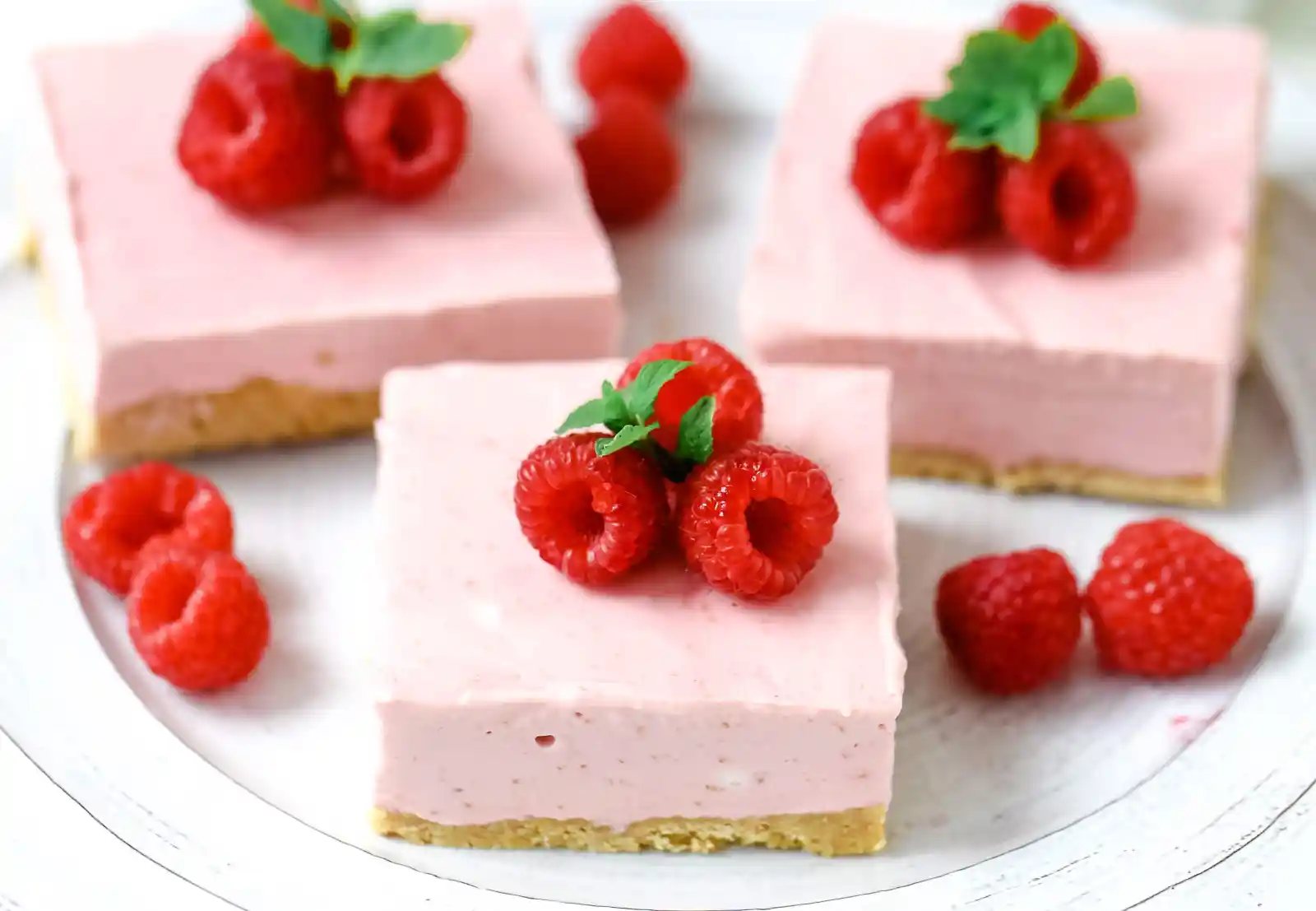 No-Bake Frozen Raspberry Cheesecake Squares. Creamy no-bake raspberry cheesecake filling on top of a shortbread or graham cracker crust topped with fresh raspberries. A creamy no-bake frozen dessert. www.modernhoney.com #nobakedessert #raspberrycheesecake #cheesecakesquares #frozendessert #frozencheesecake