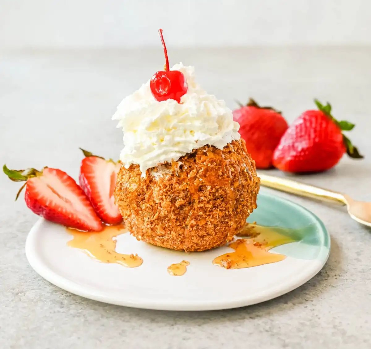 Crunchy cinnamon-sugar corn flakes coat creamy scoops of ice cream, topped with honey, whipped cream, and strawberries. This No-Fry Fried Ice Cream has zero deep-frying involved. This easy fried ice cream recipe uses corn flakes coated in buttery cinnamon sugar to mimic the crunch of a fried shell. No hot oil, no mess — just roll, freeze, and serve.