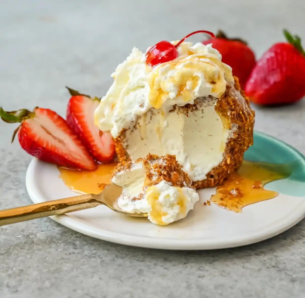 Crunchy cinnamon-sugar corn flakes coat creamy scoops of ice cream, topped with honey, whipped cream, and strawberries. This No-Fry Fried Ice Cream has zero deep-frying involved. This easy fried ice cream recipe uses corn flakes coated in buttery cinnamon sugar to mimic the crunch of a fried shell. No hot oil, no mess — just roll, freeze, and serve.