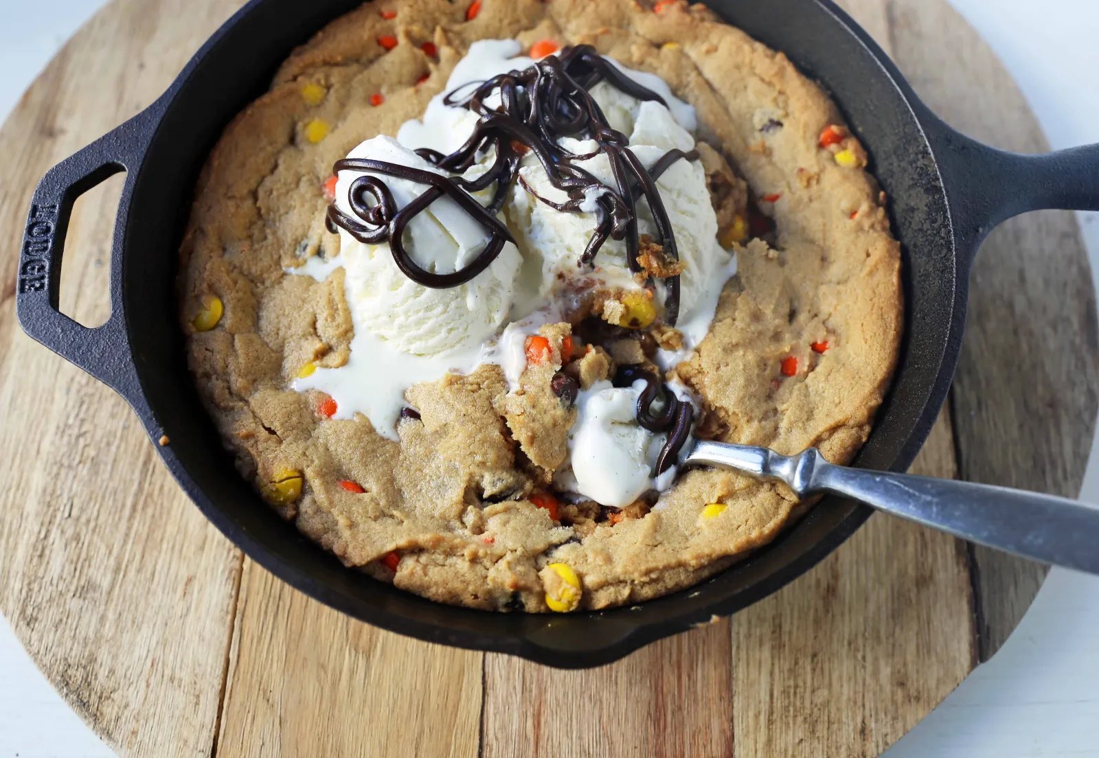 Peanut Butter Skillet Cookie. Homemade peanut butter cookie dough with Reeses Pieces baked until ooey gooey and topped with vanilla ice cream and hot fudge. www.modernhoney.com #peanutbutter #peanutbuttercookies #peanutbutterpizookie #pizookie