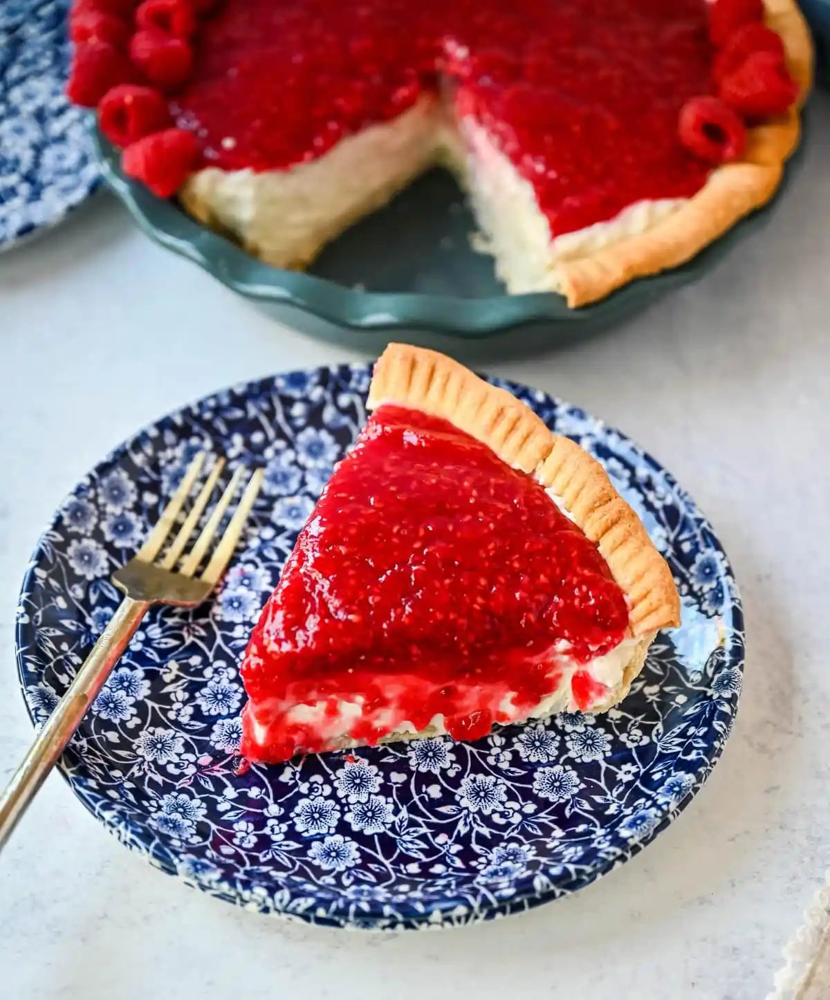 This homemade Raspberry Cream Pie is made with a sweet vanilla cream cheese cheesecake filling topped with a homemade raspberry sauce, all in a buttery, flaky homemade crust. This is a homemade take on the famous Briermere Farms raspberry cream pie and the perfect summer dessert that can be made with fresh or frozen raspberries.