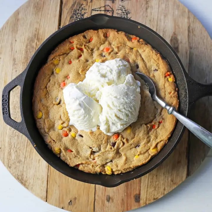 Peanut Butter Skillet Cookie. Homemade peanut butter cookie dough with Reeses Pieces baked until ooey gooey and topped with vanilla ice cream and hot fudge. www.modernhoney.com #peanutbutter #peanutbuttercookies #peanutbutterpizookie #pizookie