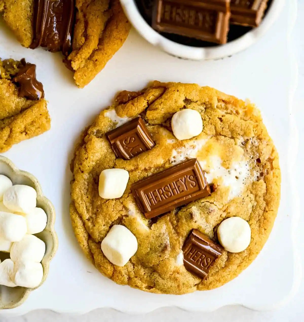These homemade s'mores cookies are thick, soft, and chewy with gooey marshmallow bits and chopped Hershey bar throughout every bite. A full cup of finely crushed graham cracker crumbs goes straight into the dough, giving these cookies that unmistakable campfire s'mores flavor! This easy s'mores cookie recipe comes together in one bowl and is ready from start to finish in about 30 minutes.