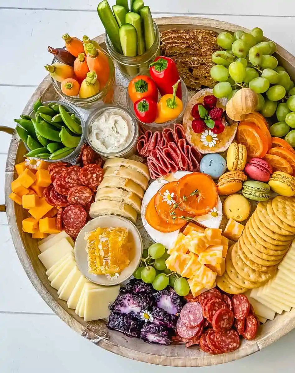 A beautiful Spring Charcuterie Board with fresh ripe fruits, creamy cheeses, crisp vegetables, cured meats, crackers, French baguette slices, honeycomb, macarons, and edible flowers. This is a perfect Spring entertaining board.