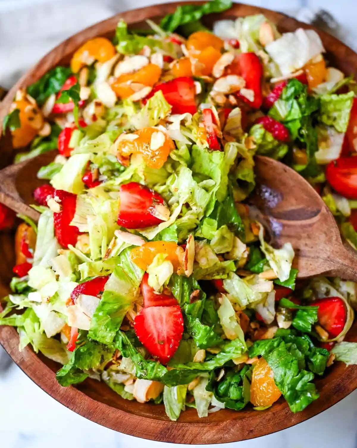 A fresh strawberry mandarin orange salad with candied almonds is the perfect summer side dish! Sweet strawberries, mandarin oranges, crunchy candied almonds, and a light homemade dressing.