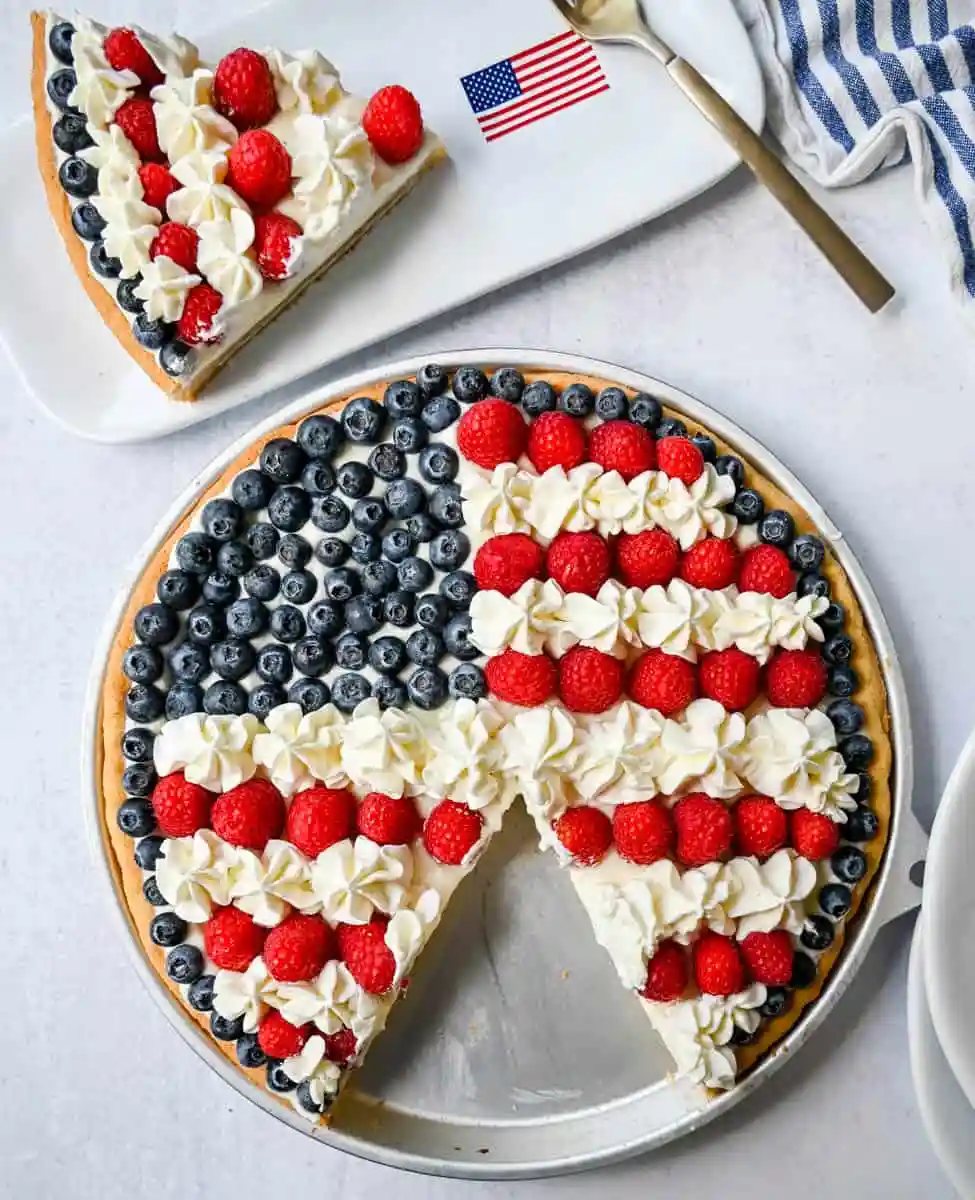 This flag sugar cookie fruit pizza is a festive, delicious, and beautiful patriotic 4th of July dessert featuring a homemade soft sugar cookie crust with a sweet vanilla cream cheese frosting topped with fresh raspberries, blueberries, and homemade whipped cream.