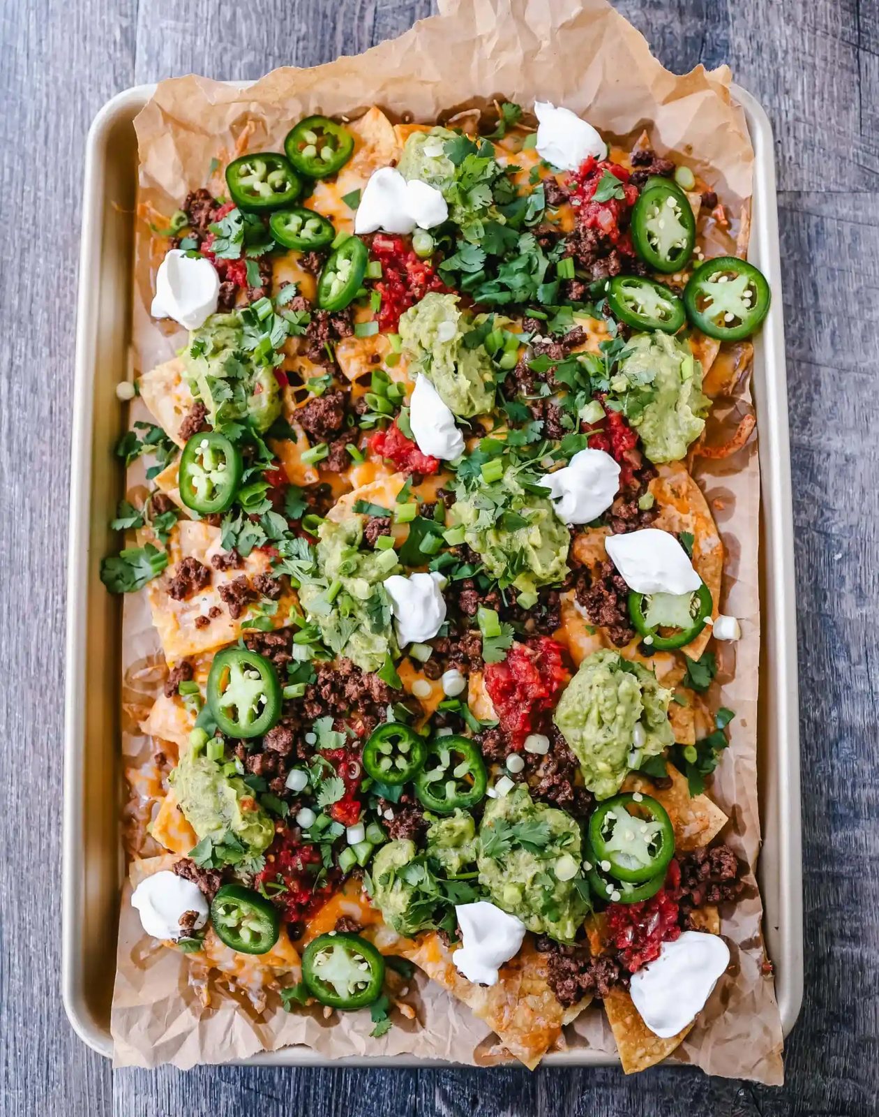 Ground Beef Nachos Recipe Seasoned ground beef with crispy tortilla chips, Mexican cheeses, fresh guacamole, sour cream, jalapenos, fresh salsa, green onions, and cilantro make the best beef nachos!