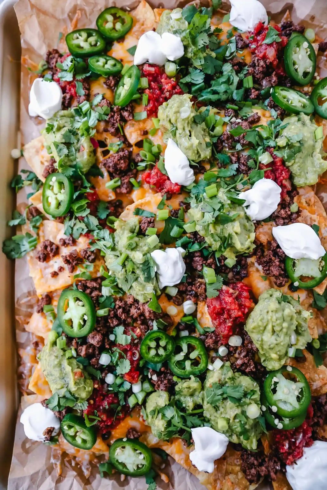 Ground Beef Nachos Recipe Seasoned ground beef with crispy tortilla chips, Mexican cheeses, fresh guacamole, sour cream, jalapenos, fresh salsa, green onions, and cilantro make the best beef nachos!