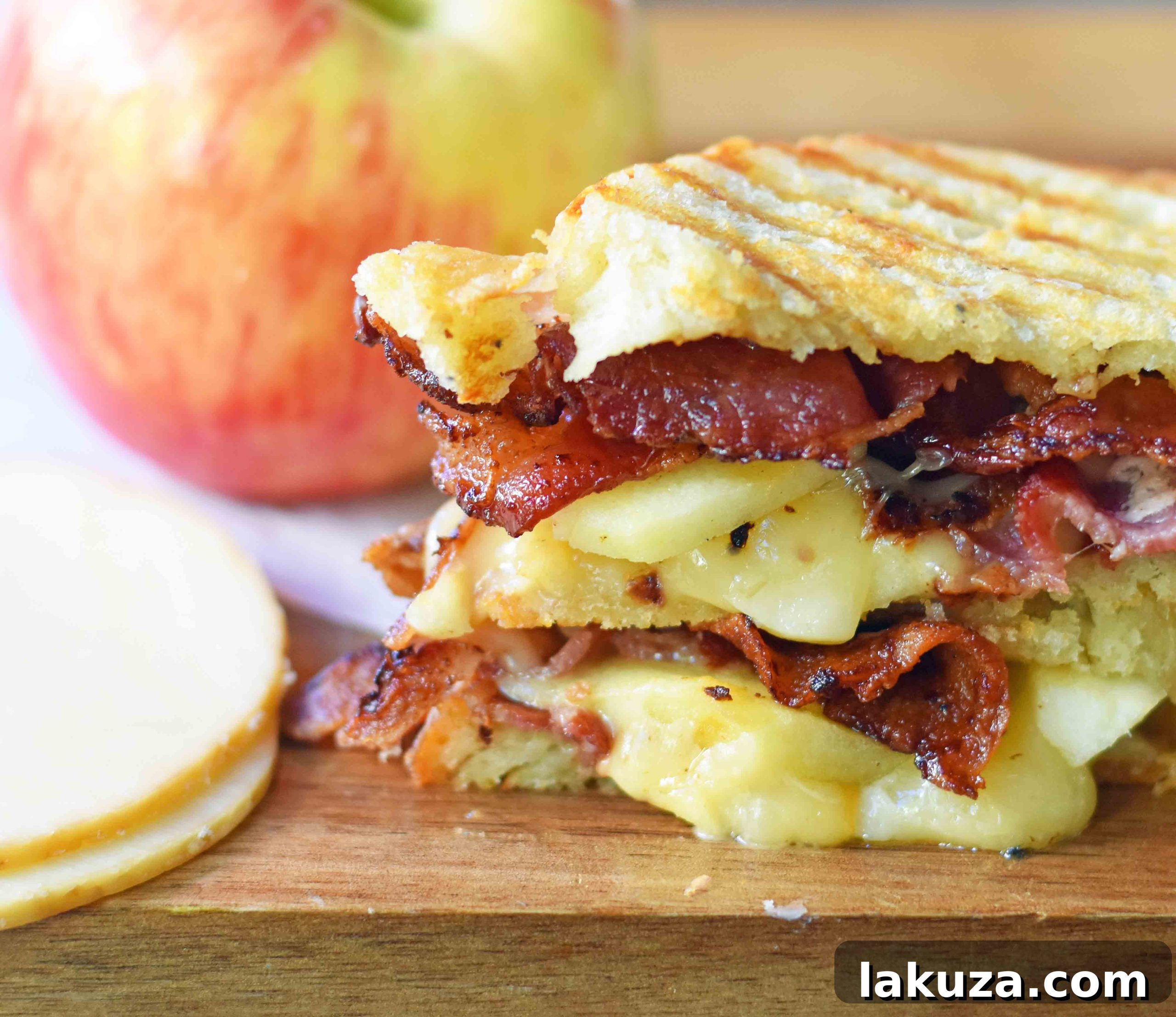 Honeycrisp Apple & Smoky Bacon Gouda Melt 5 Close-up of a cut gourmet grilled cheese sandwich, revealing melted smoked gouda cheese, apple slices, and bacon between sourdough bread.
