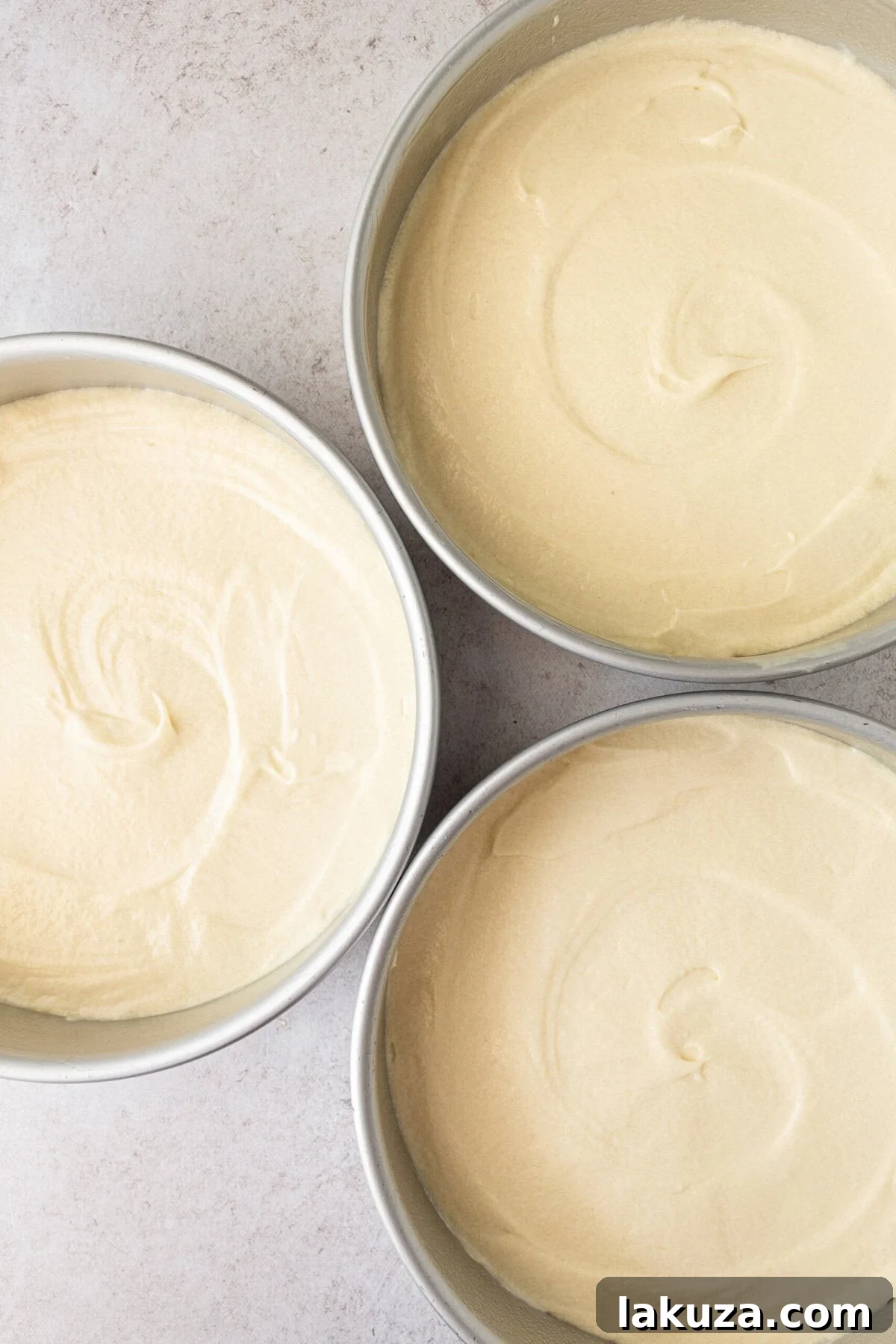 Three 8-inch cake pans filled with smooth coconut cake batter, ready for baking to create a multi-layered cake.