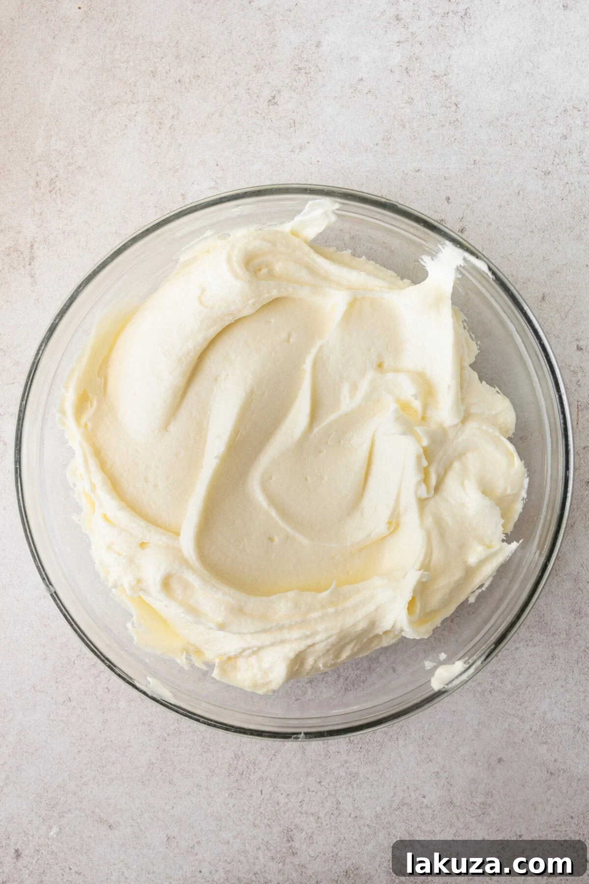 Creamy, fluffy coconut cream cheese frosting spread generously onto a homemade coconut cake layer, ready for assembly.