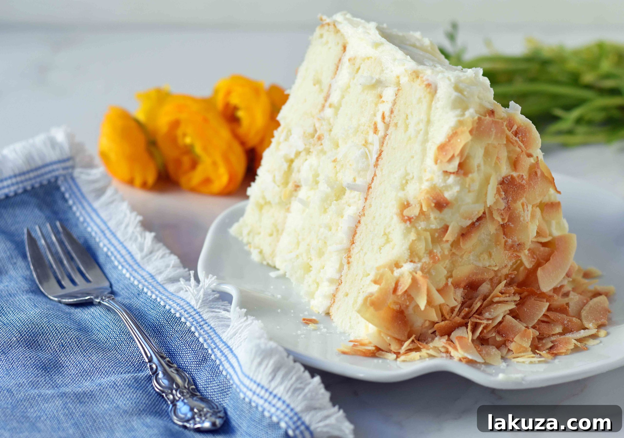 A close-up view of the exterior of a homemade coconut cake, beautifully frosted with coconut cream cheese and adorned with coconut flakes, ready for a festive occasion.