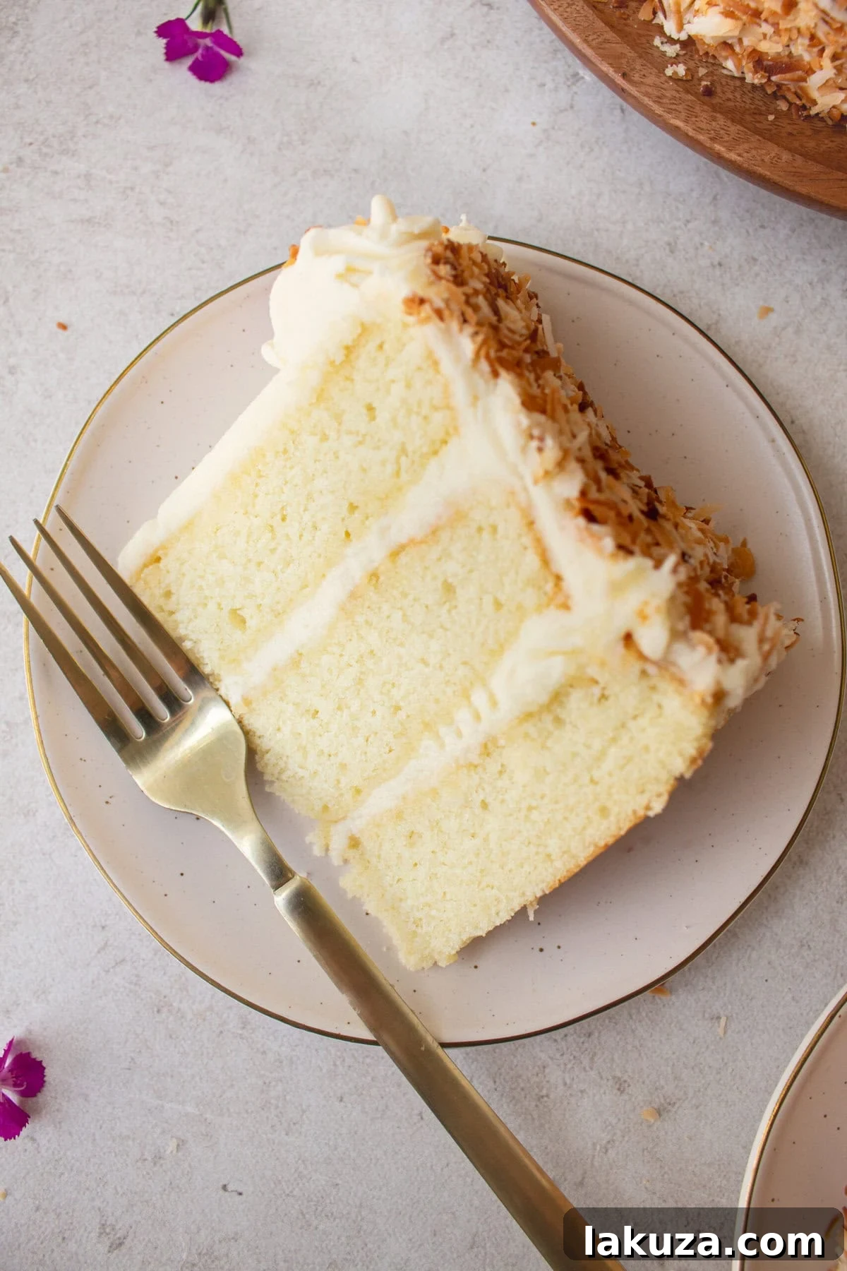 A slice of moist coconut cake drizzled with a simple syrup, enhancing its tenderness and flavor. This homemade layered cake is a perfect dessert.