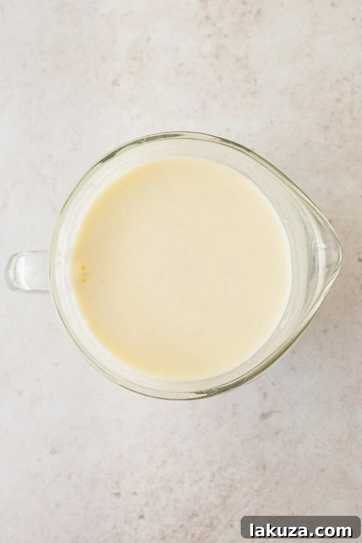A bowl of wet ingredients for coconut cake, including creamy coconut milk and tangy buttermilk, ready to be added to the dry mixture.