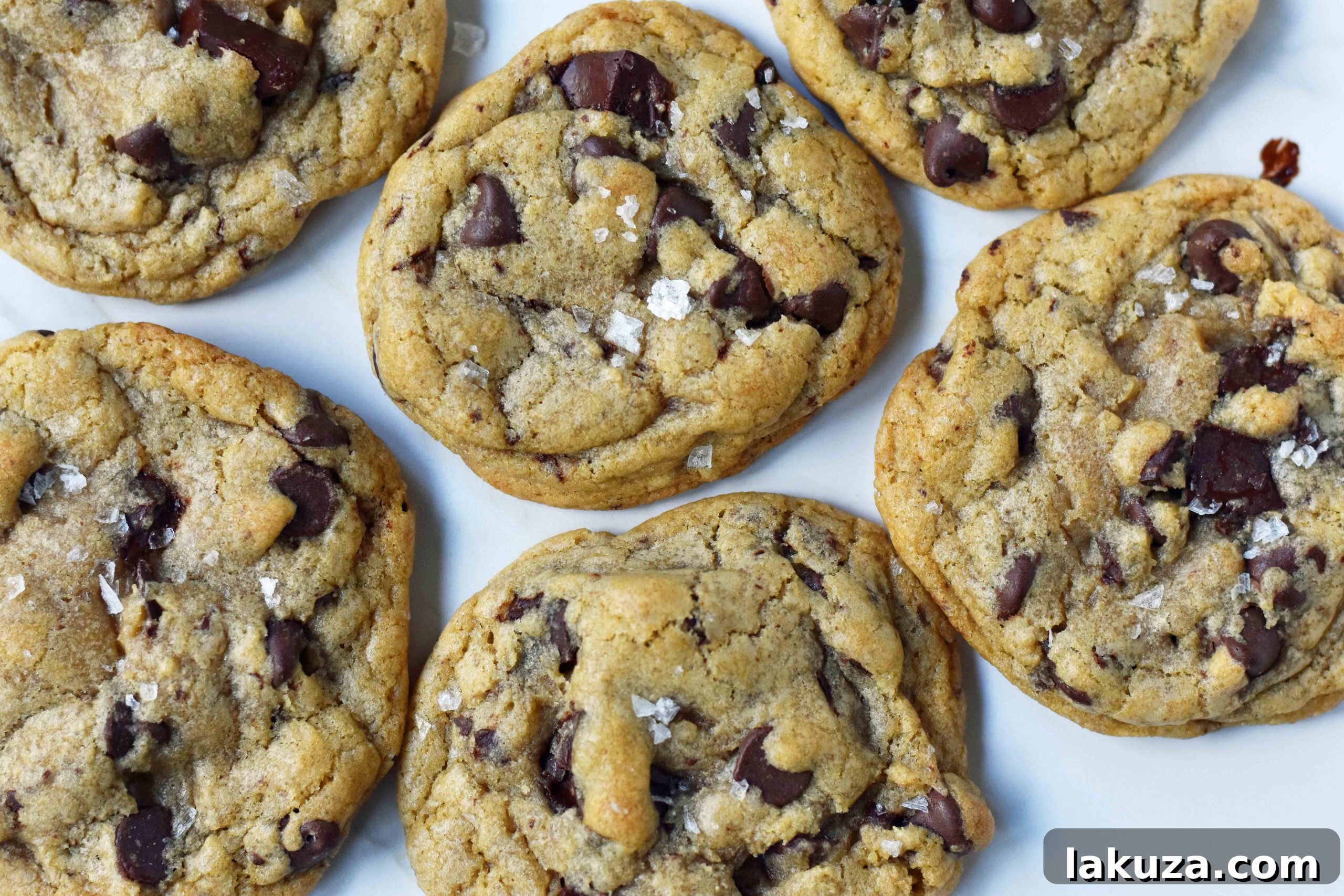 Rich Dark Chocolate Olive Oil Cookies 4 A stack of Dark Chocolate Chunk Olive Oil Cookies with a sprinkle of sea salt on a wooden surface.
