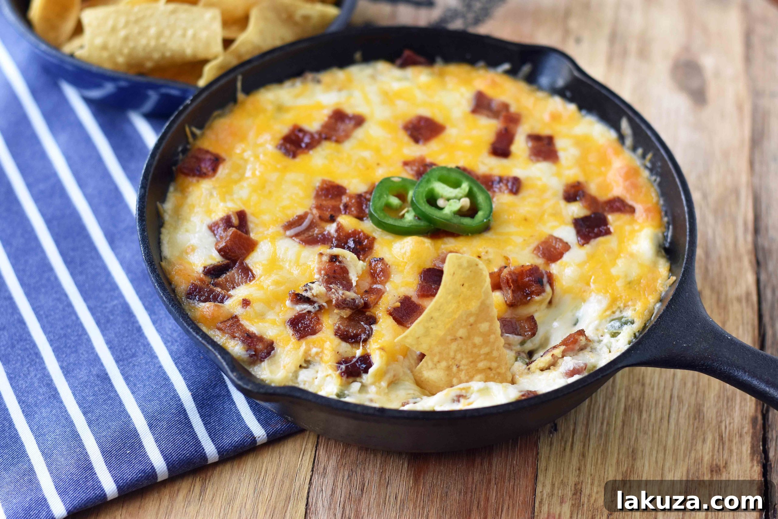 A close-up of a serving of Creamy Jalapeno Popper Dip with Bacon in a white bowl, garnished with fresh cilantro and surrounded by tortilla chips.