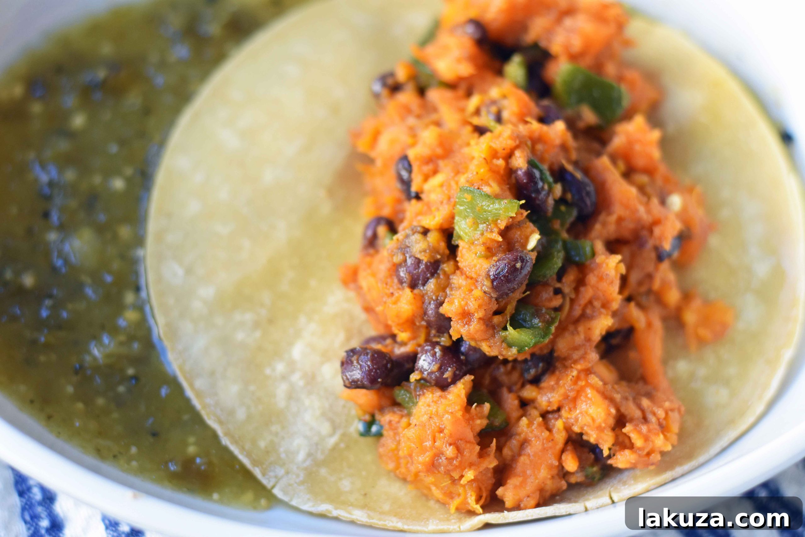 Zesty Sweet Potato and Black Bean Enchiladas 6 Hands carefully rolling the sweet potato and black bean filling into a warm corn tortilla, demonstrating the assembly process of the enchiladas.