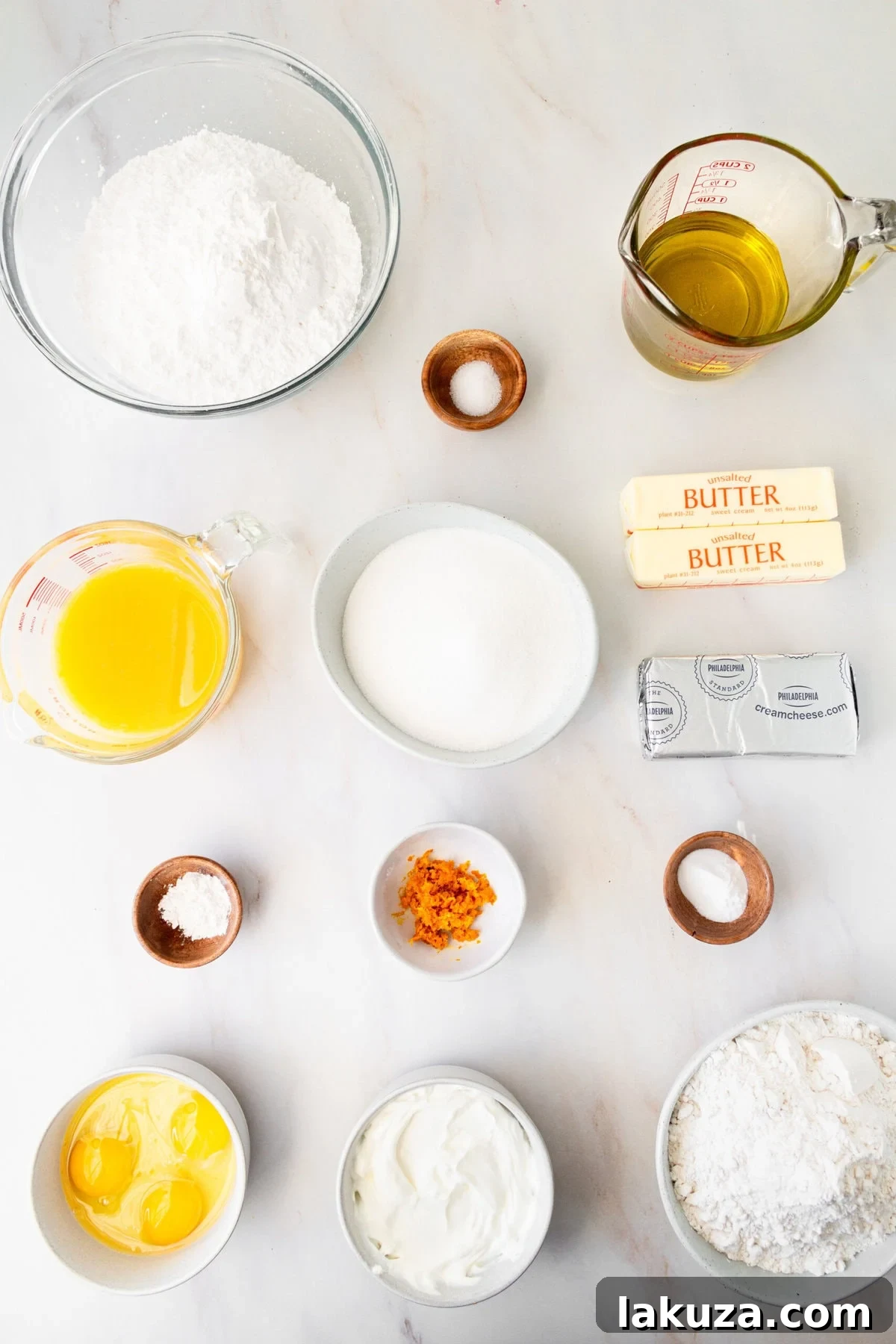 Zesty Orange Dream Cake 4 A flat lay of fresh orange cake ingredients, including flour, sugar, fresh oranges, eggs, sour cream, butter, and cream cheese. These are the key ingredients needed to make a homemade orange cake with orange cream cheese frosting.