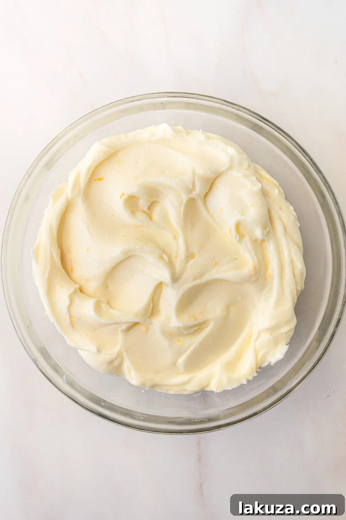Zesty Orange Dream Cake 8 A bowl of creamy, sweet orange cream cheese frosting, ready to be spread over a homemade orange cake, capturing its smooth texture and light orange hue.