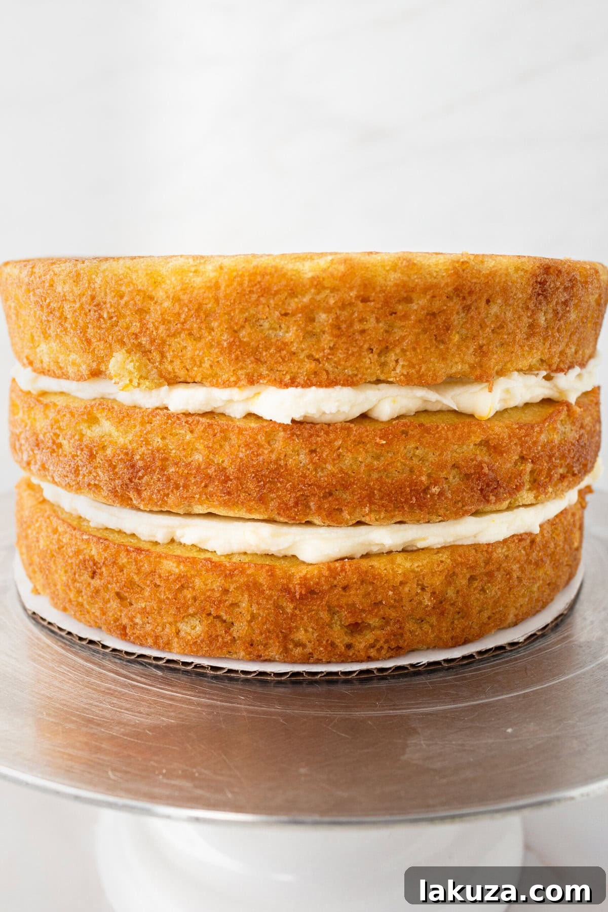 Zesty Orange Dream Cake 9 An offset spatula expertly applying a thin layer of orange cream cheese frosting to the sides of a tiered orange naked cake, revealing its beautiful layers beneath.