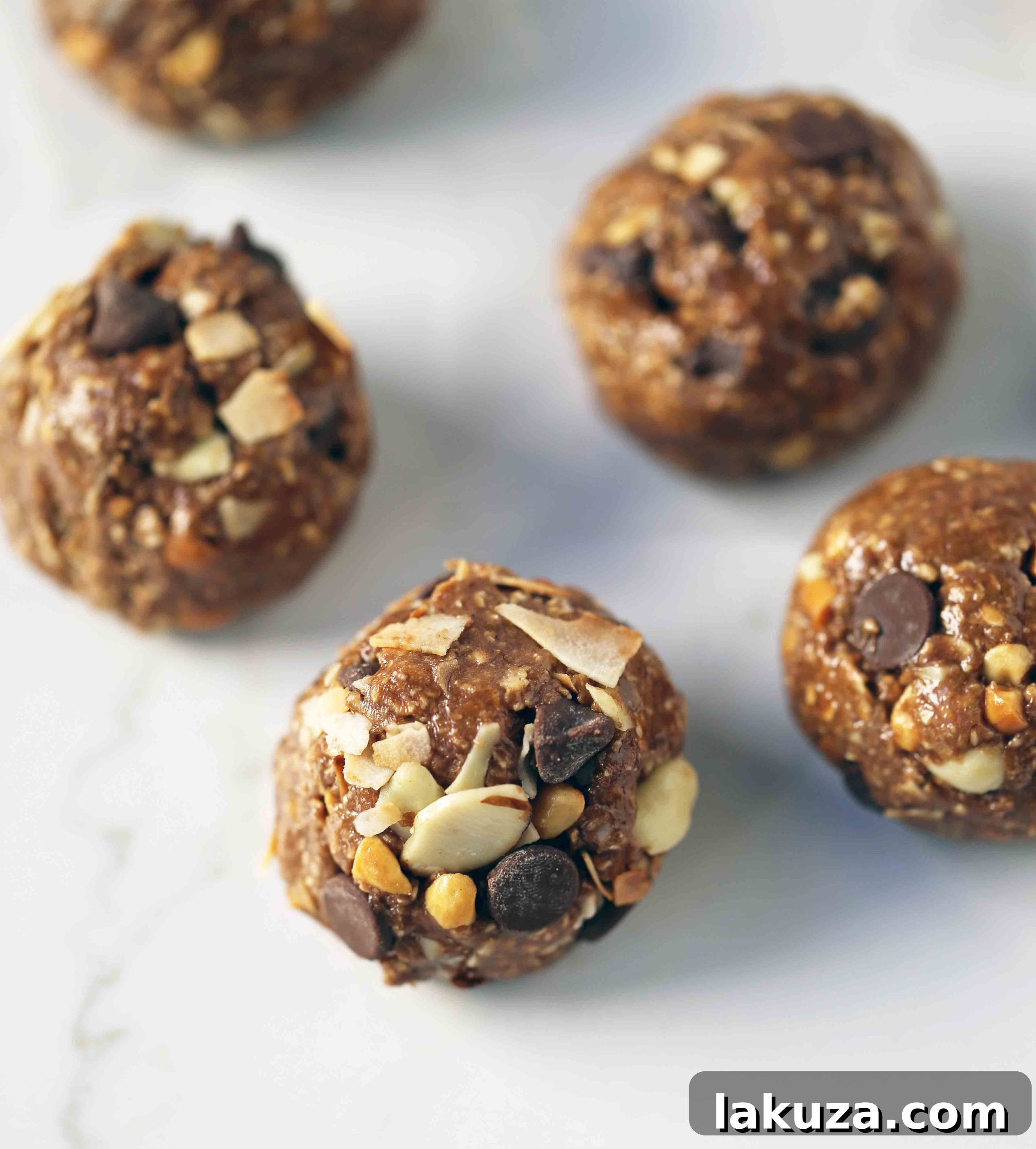 A close-up of a hand rolling no-bake protein energy balls, with a baking sheet filled with finished balls in the background. Demonstrates the ease of preparation.