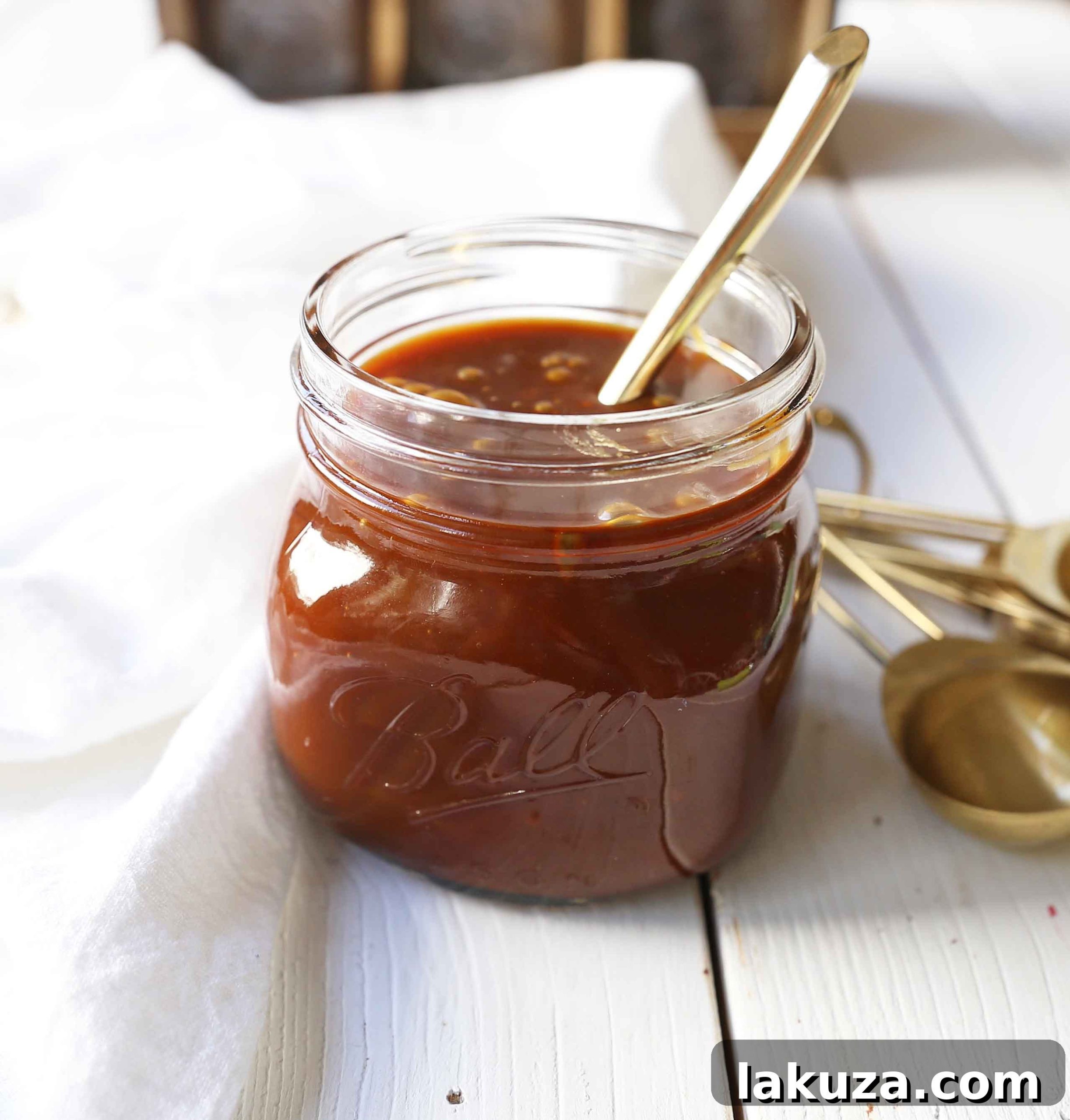 Closeup of homemade salted caramel sauce bubbling gently in a heavy-bottomed saucepan, with a wooden spoon nearby.