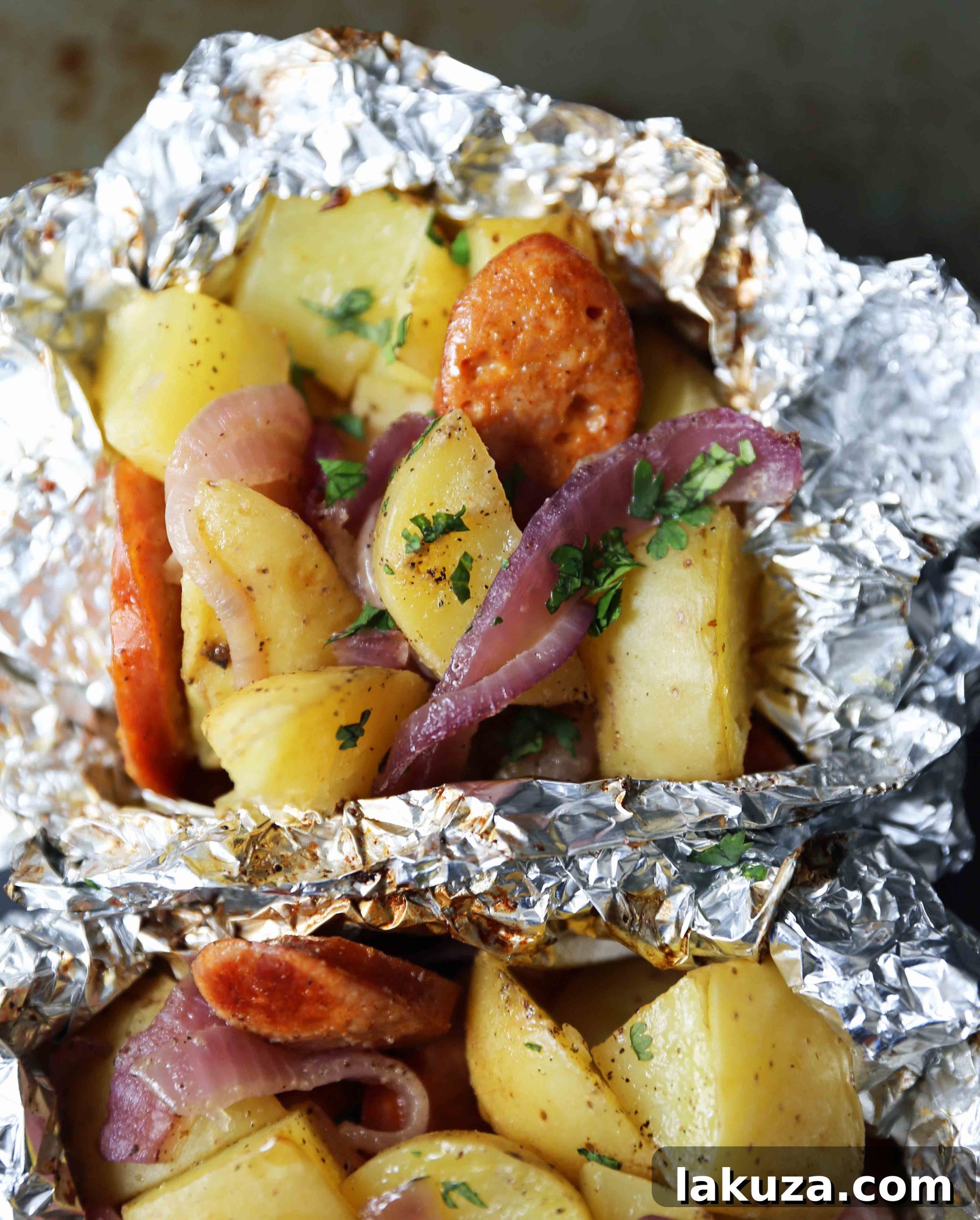 Hearty Sausage and Potato Foil Meals 4 Uncooked Sausage Potato Foil Packets showing sliced smoked sausage, cubed gold potatoes, and thinly sliced red onions seasoned and ready to be sealed. An easy and flavorful tin-foil dinner for the oven or grill. #sausagepotatoes #foilpacketrecipe #simpledinner #mealprep
