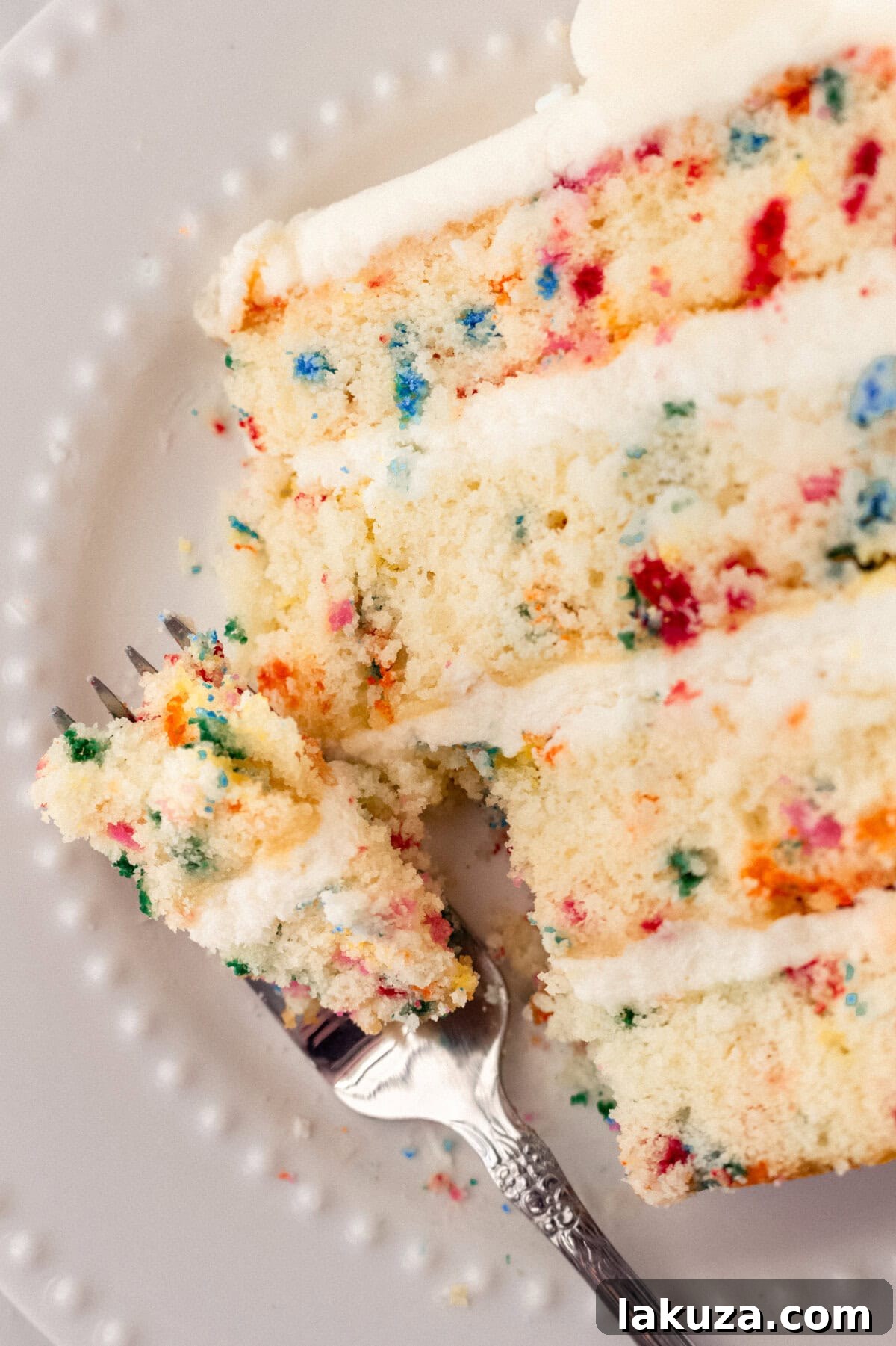 Joyful Sprinkle Celebration 13 A beautifully completed homemade Funfetti cake, lavishly frosted with creamy buttercream and adorned with a delightful assortment of rainbow sprinkles, ready to be served.
